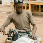 A skilled tailor sewing clothes on a traditional sewing machine on a Kumasi street.